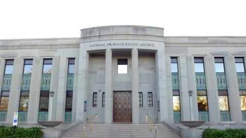 Art Deco NFSA building from front view, with blue sky in the background and flags flying atop of the building