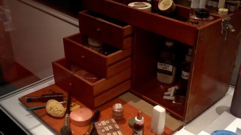 Wooden make-up chest belonging to film make-up artist Vivien Mepham. The chest's drawers are open and make-up jars, brushes and bottles are displayed in front of the chest