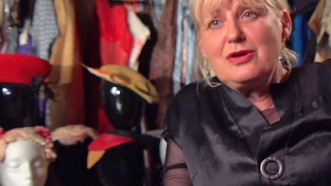 Costume designer Marion Boyce pictured sitting down surrounded by dresses and costume accessories.