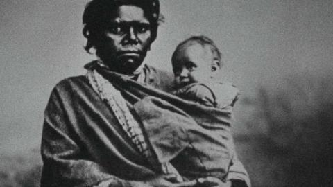 A black-and-white photo dating from the early 20th century of an Indigenous woman holding a baby.