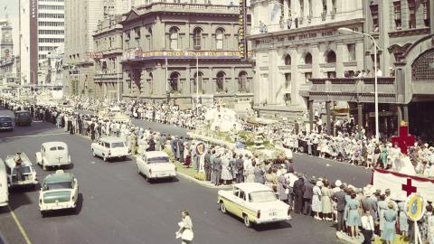 A main street of Adelaide lined with people and cars during a festival. 
