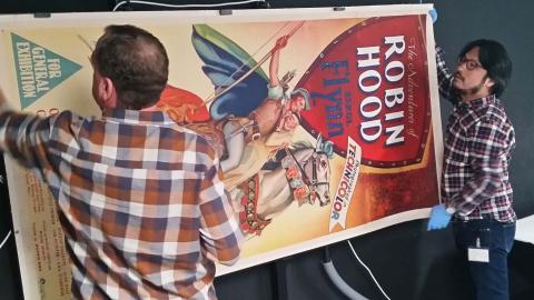 Two NFSA staff members carrying a poster for the film The Adventures of Robin Hood, starring Errol Flynn
