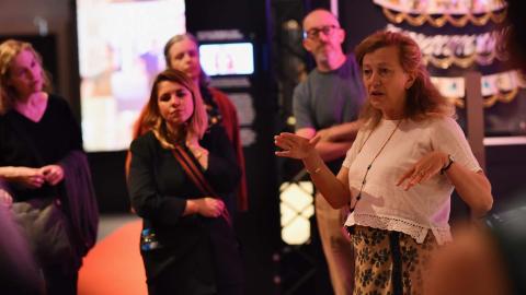 A female tour guide discussing an exhibition to a small group of interested onlookers in the gallery of the National Film and Sound Archive