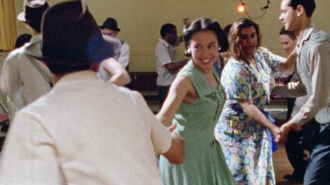 A mix of white and First Nations people dressed in 1950s clothes dancing together. 