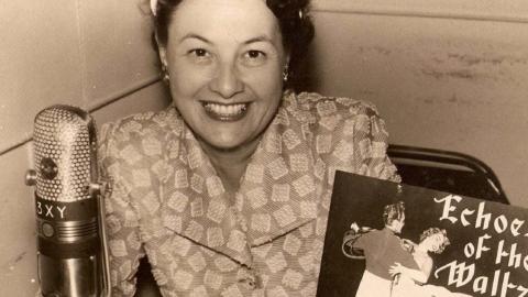 Radio personality Binny Lum behind the microphone at Radio 3XY in the 1950s or 1960s. She holds a vinyl record labelled Echoes of the Waltz.