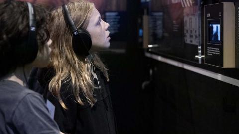 A young girl wearing headphones is looking at a screen in a gallery space at the NFSA