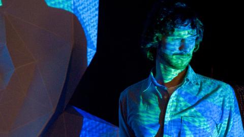 Man with blue green yellow projection over his face. 