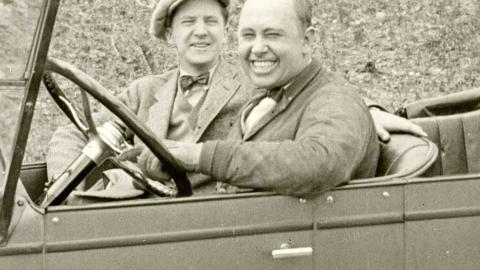 Two men sitting in a motor car and smiling at the camera, c1924.