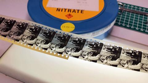 A strip of film negatives laid out on a table before a can of flammable nitrate film