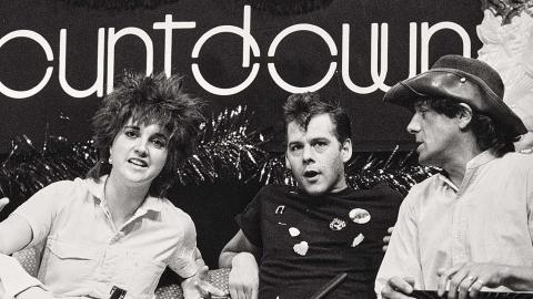 A woman and two men sitting on a couch under a sign that says 'countdown'