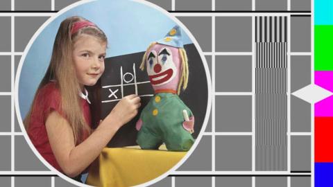 A colour TV test pattern with an inset image of a young girl in front of a chalkboard with a toy clown beside her