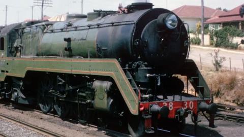 A steam train on a track in a suburban area.