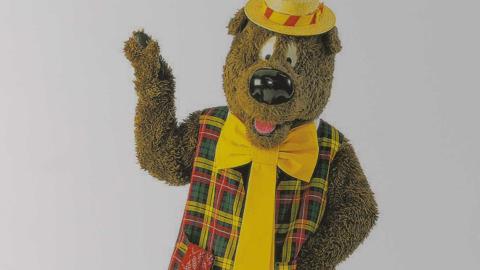 Upper body image of children's TV character Humphrey B. Bear wearing a plaid vest, yellow tie and boater hat.