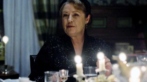 Actor Noni Hazelhurst dressed in black and seated at a dinner table in a scene from the show A Place to Call Home
