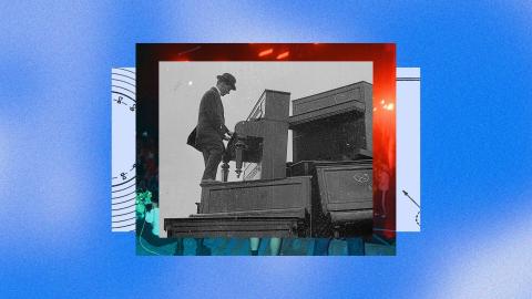 A man in a suit and bowler hat plays an upright piano while standing on another piano