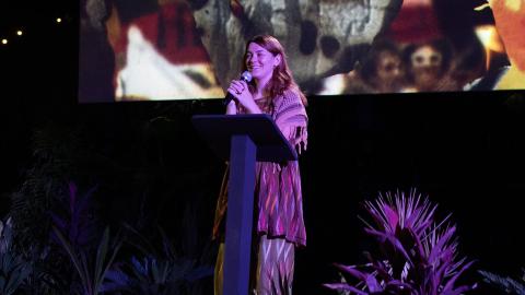 Jazz Money standing at a lectern in front of a cinema screen displaying an image from their film WINHANGANHA