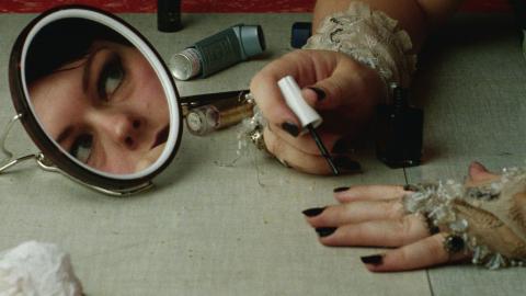 Genevieve Lemon's face is reflected in a small mirror while she applies black fingernail polish.