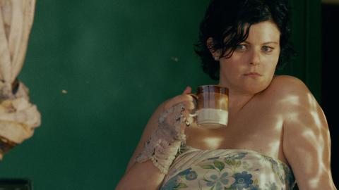 Genevieve Lemon holding a coffee mug and looking out the window in a still from the film Sweetie.