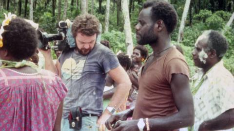 Co-director Chris Owen holds a film camera on his shoulder and stands next to co-director and star Albert Toro and other actors on location for the 1982 film Tukana in the Papua New Guinea Highlands.