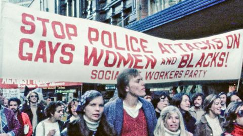 A Sydney protest march in the late 1970s with young people walking under a banner that reads 'Stop police attacks on gays, women and blacks!'