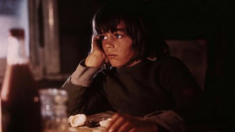 Production still of young Greg Rowe as Storm Boy sitting in his darkened humpy. His face is lit by a lamp.  