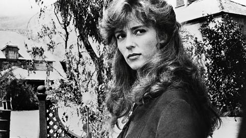 Rachel Ward holds a rose and turns her head to look at the camera in a scene from The Thorn Birds