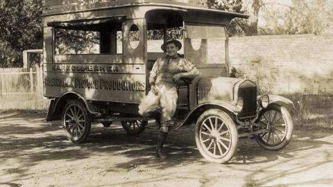 Actor and filmmaker Snowy Baker leaning against a car with 'Carroll-Baker Australian Picture Productions' written on the side