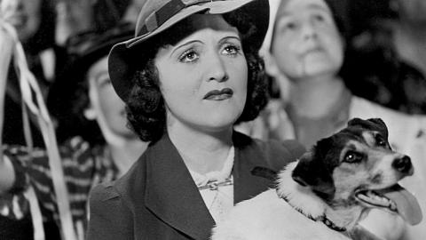 A crying Diana Du Cane holds a dog in her arms and looks upwards at a departing ship in a scene from The Broken Melody
