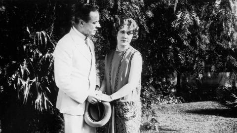 A man holds hands with Louise Lovely in a garden in a scene from the silent film Jewelled Nights.