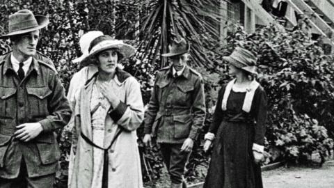Two Australian soldiers from the First World War walk in uniform, accompanied by three women