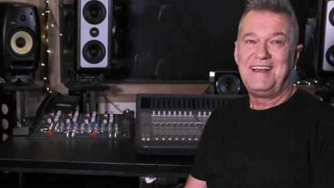 Singer Jimmy Barnes pictured from the chest up, in a black t-shirt and sitting in front of a mixing deck in a recording studio. 
