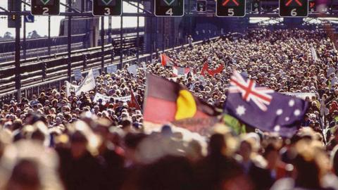 Huge crowd on the Sydney Harbour Bridge during the Walk for Reconciliation. Some people are waving Australian and Aboriginal flags. 
