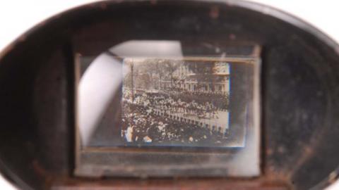 Looking through the viewing lens of a kinora at an image of a crowd scene.