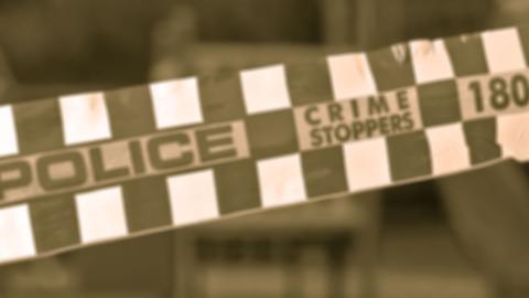 A sepia-toned shot of some checkered police tape with the words Police and Crime Stoppers written on it.