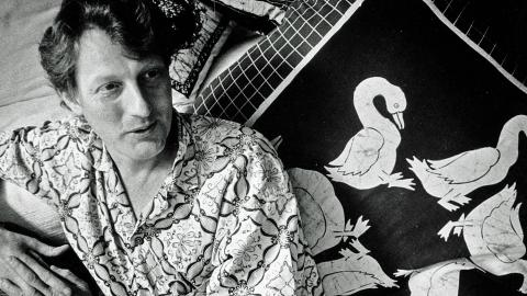 Australian documentary filmmaker, John Darling, pictured from waist up, wearing a Balinese shirt and leading against a cushion with images of birds on it.