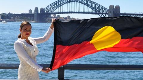 Cheree Toka holding an Australian Aboriginal flag. The Sydney Harbour Bridge is in the background.
