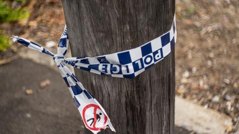 True Crime - Police tape A section of a telegraph pole on a sidewalk with some blue and white chequered police tape tied around it.