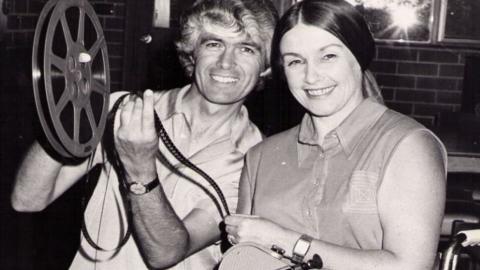 Don and Barbara Worley, 1975. Don holds film reel and Barbara is sitting in wheelchair holding movie camera.