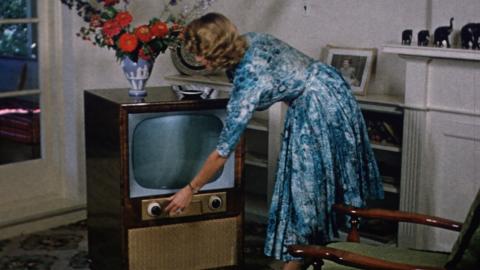 1950s image of a woman turning on a television set in her living room.