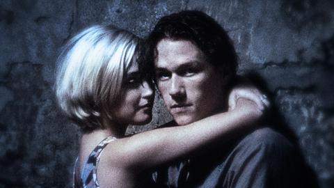 Heath Ledger as Jimmy and Rose Byrne as Alex in a still from Two Hands. The shot is grainy and plays with focus. They are in an embrace while they lean on a wall. Ledger looks at the camera.