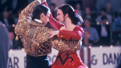 Paul Mercurio and Tara Morice in a scene from the film Strictly Ballroom. The are pictured from the waist up in a dancing pose and wearing Spanish-style costumes.