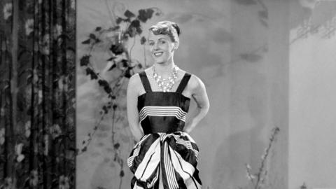 A woman is modelling a dress. She is looking at the camera.