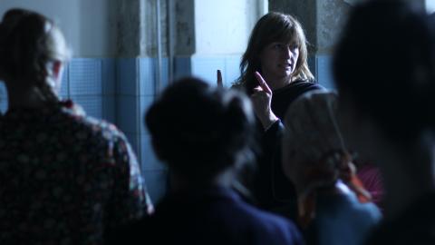 Director Cate Shortland directs a room full of people. We see the other people from behind and out of focus.