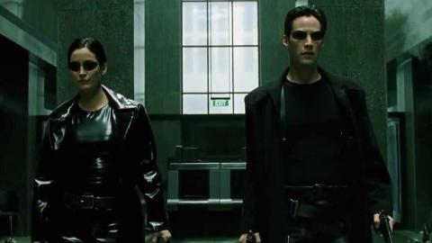 A man and a woman wearing dark sunglasses, black clothes and carrying guns.