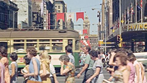 A busy street in Melbourne city with pedestrians and a tram going past.