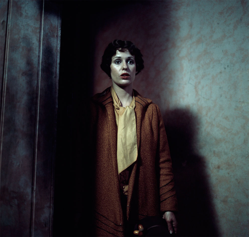 Film still of Helen Morse as Caddie walking into a dark room with a look of apprehension.