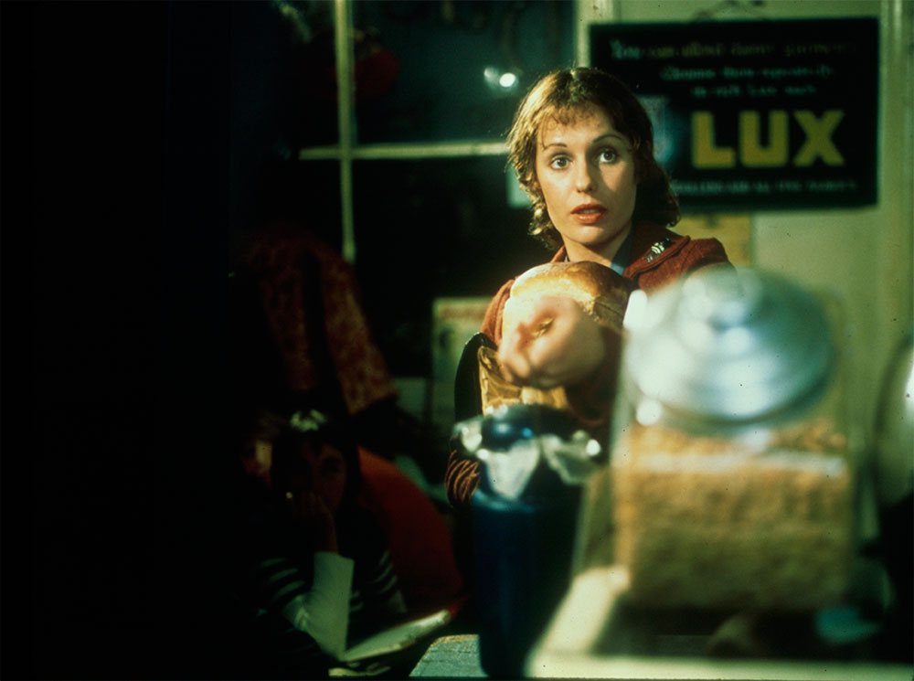 Film still of Helem Morse as Caddie seated in a shop holding one of her on screen children in her lap.